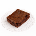 A deep, rich colored brownie filled with air pockets to emphasize its fluffier texture, along with chocolate chips visible throughout the treat, presented on a white lace doily with a white background.