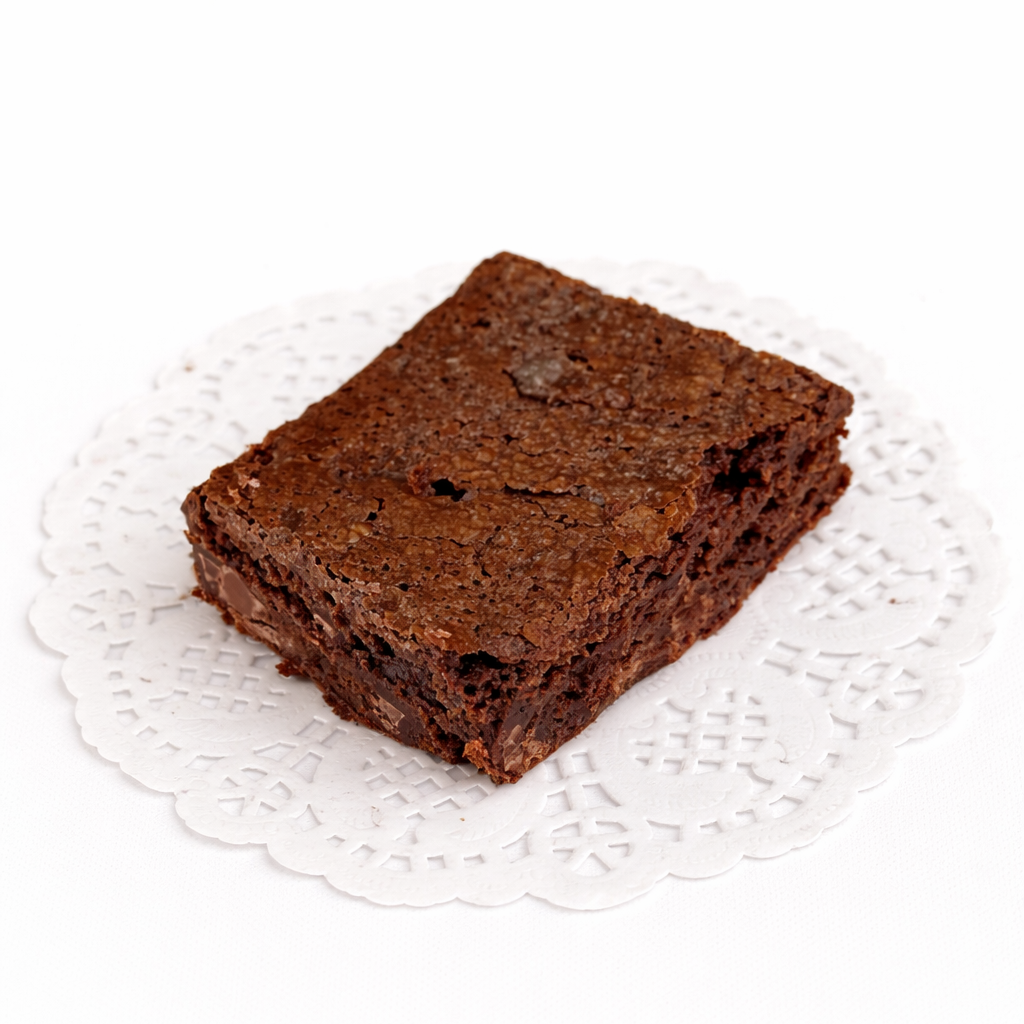 A deep, rich colored brownie filled with air pockets to emphasize its fluffier texture, along with chocolate chips visible throughout the treat, presented on a white lace doily with a white background.