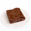 A dense brownie with a light, crispy lamination across the top, with chocolate chips clearly baked throughout it, presented on a white doily with a white background.